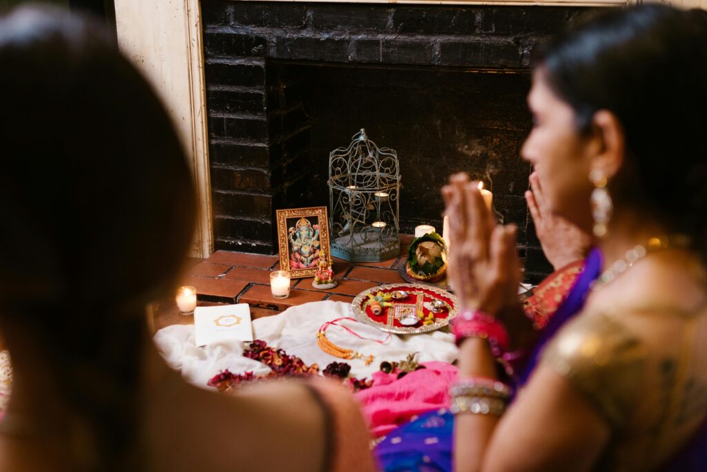 pexels-photo-7685985-7685985-1 Two women engaged in prayer at a Hindu altar, adorned with candles and traditional offerings, showcasing spirituality and culture.