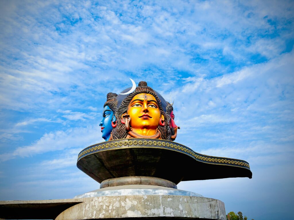 pexels-photo-33372656-33372656 Vibrant three-headed Shiva statue under a blue sky in Pokhara, Nepal.
